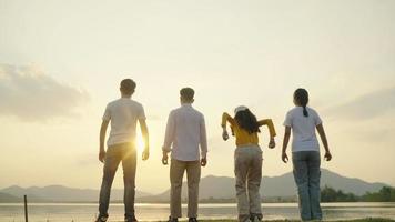 Four People Group of happy teenagers raising hands jumping on sunset mountain and river background. video