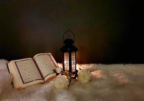 The lantern of Ramadan is black in color, luminous, decorated with wooden motifs, next to the Holy Quran, with a few white roses photo