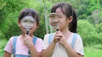 Children learn and explore nature with an outdoor magnifying glass. Curious child looks through a magnifying glass at the trees in the park. Two little sisters playing with magnifying glass. video