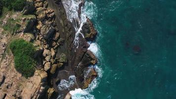 aereo superiore Visualizza 4k metraggio di fuco di oceano blu onde rompere su alto scogliera di un' roccioso montagna. Pericolo mare onde su un' spiaggia video