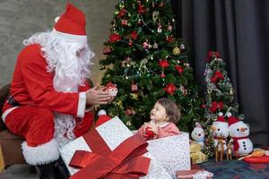 Caucasian baby is getting present from Santa claus at night by the fully decorated christmas tree for season celebration concept photo