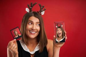 Woman in Christmas mood comparing instant pictures to smartphone camera over red photo