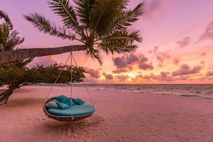Romantic beach sunset. Palm tree with swing hanging before majestic clouds sky. Dream nature landscape, tropical island paradise, couple destination. Love coast, closeup sea sand. Relax pristine beach photo