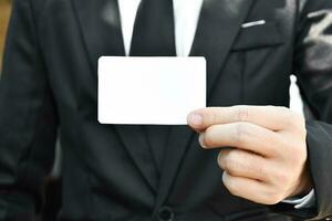 Closeup of businessman who takes out white piece of paper from the pocket in black suit. Idea for business credit card or visiting card. photo