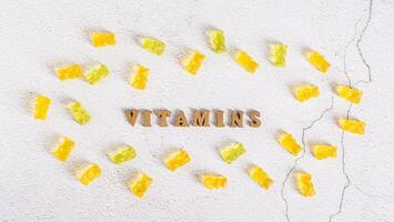 The word vitamins from letters and gummy vitamins in the form of candy bears around top view photo