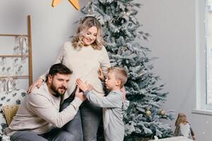 Christmas Family Happiness Portrait of dad, pregnant mom and little son  sitting armchair at home near Christmas tree hug smile photo