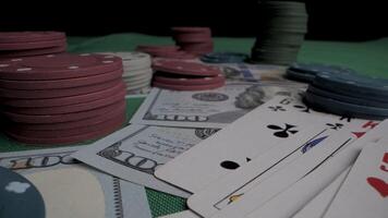 een detailopname schot van een groen voelde tafel met stapels van poker chips, kaarten en contant geld verspreide aan de overkant haar oppervlak. de chips zijn in verschillend kleuren, en de contant geld is in ons dollar. video