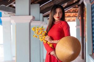 Vietnamese girl with Ao Dai dress standing in traditional house of Vietnam. Text in photo mean best wishes to family, happiness, prosperity, health. Tet holiday and New Year.