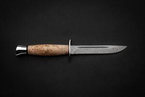 Damascus hunting knife with a wooden handle on a dark background. Melee weapons for hunting and self-defense. The instrument of crime. photo