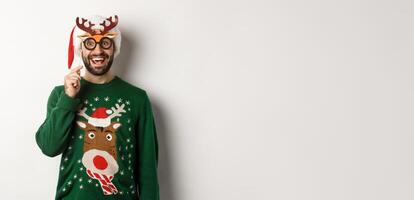 Christmas and holidays concept. Happy bearded man celebrating xmas, holding party mask and wearing Santa hat, smiling amazed, standing over white background photo