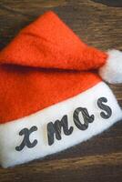 A little Santa hat with the letters Xmas on it. On a wooden background. background for Christmas. photo