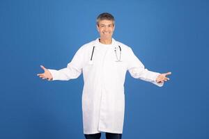 A mature Caucasian man in a white lab coat stands with open arms, smiling confidently. He represents a general physician, embodying the spirit of healthcare and professionalism. photo