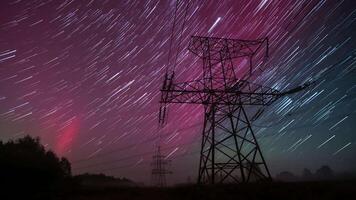 Long exposure captures the rhythmic dance of stars and auroras above towering power lines in a tranquil rural landscape under a stunning night sky filled with vibrant colors. video