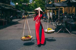 A young woman in a Vietnamese outfit carries a fruit basket in the ancient city of Hoi An in Vietnam. photo