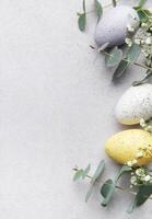 Easter eggs and leaves forming a frame on gray background photo