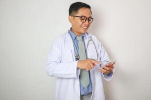 Male doctor asian wears a blue shirt with a headset in his pocket, using a modern smart phone device with touch screen in hospital. Healthcare and medical concept. photo